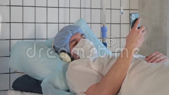年轻男性病人躺在医院的床上用耳机听音乐视频的预览图