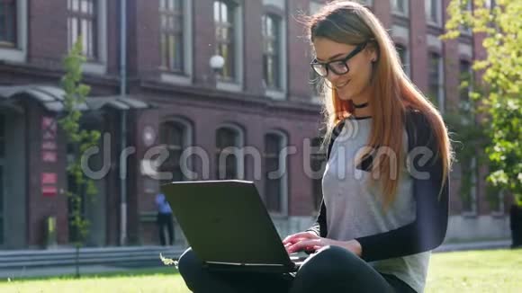 快乐而现代的女学生或自由职业者在笔记本电脑上工作坐在校园绿色草坪上的公园里视频的预览图