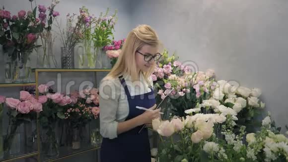 鲜花店花卉精品店女小企业主的肖像微笑着在温室里检查鲜花视频的预览图