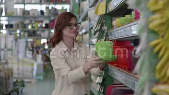 可爱的戴眼镜微笑的女人在百货商店买彩色花盆给家里的花匠设计视频的预览图