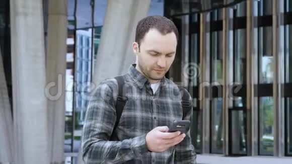 休闲男子走在现代建筑附近用微笑的手机视频的预览图