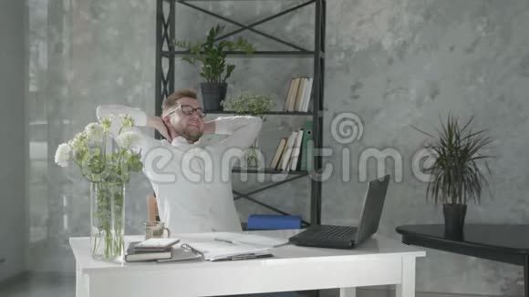 在一间现代化的办公室里一个快乐的男人手拉着手坐在桌子旁边的椅子上手里拿着电脑视频的预览图