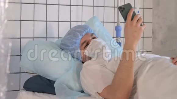 男性患者在医院卧床休息时手持手机视频的预览图