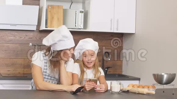 可爱的快乐姐妹扮成厨师在智能手机上浏览各种馅饼食谱视频的预览图
