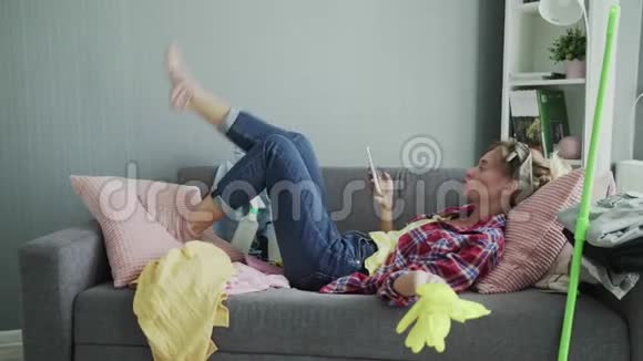 年轻女子正在使用电话在打扫完房子后休息在沙发上视频的预览图