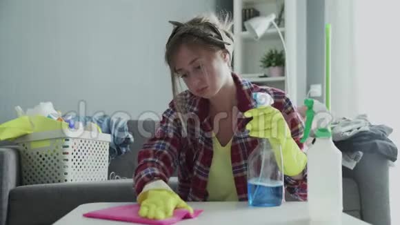 一个疲惫的女人用粉色的海绵努力清除桌子上的灰尘视频的预览图