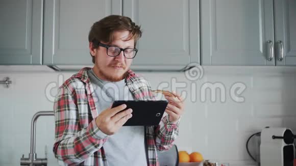 带着药片的年轻人吃巧克力糊的吐司男人在平板电脑上看有趣的视频笑视频的预览图