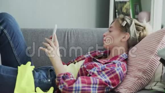 年轻女子正在使用电话在打扫完房子后休息在沙发上视频的预览图