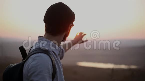 自信的年轻人的肖像戴着圆形太阳镜黑豆帽和背包背景是日落视频的预览图