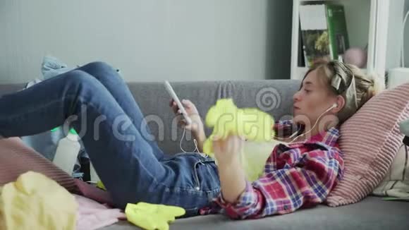 年轻女子正在听音乐打扫完房子后躺在沙发上休息视频的预览图