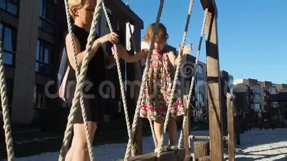 一个小女孩走在儿童游乐场电缆桥上妈妈帮她慢动作视频的预览图