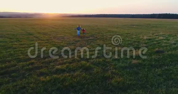 年轻的母亲带着女儿在夕阳下的田野里走着手牵手跑着空中观景视频的预览图