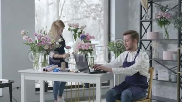 花店一男一女员工看着便携式电脑的展示接受客户的鲜花订单视频的预览图