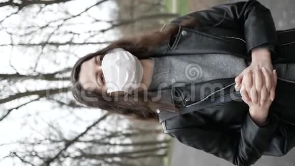 戴面具的年轻女子在城里的公园里她咳嗽大流行性冠状病毒垂直视频视频的预览图