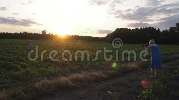 摄影师一个女人在日落时在田野里拍摄一个十几岁的女孩视频的预览图