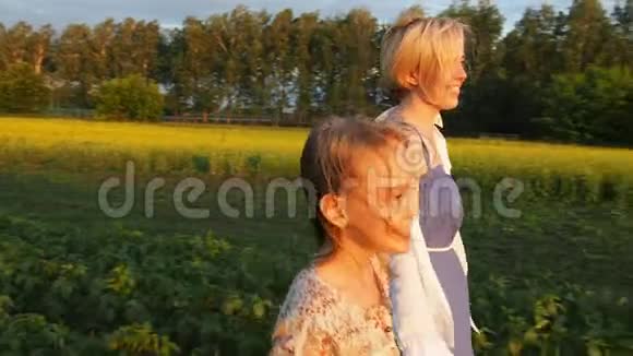 母亲和女儿在日落时穿过种植园快乐的人慢动作视频的预览图