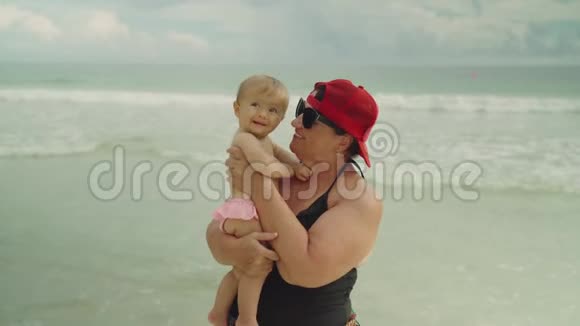 快乐的祖母在海滩上抱着她的小孙子背景是大海视频的预览图