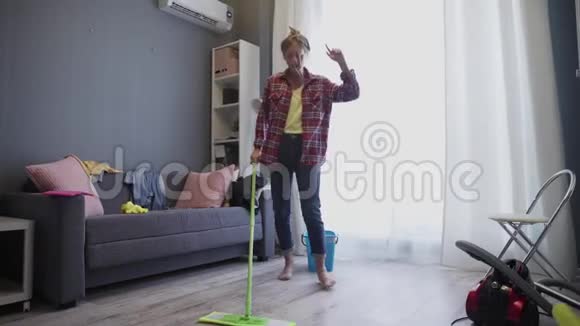 快乐的年轻女人可爱的家庭主妇用拖把洗地板在家跳舞视频的预览图