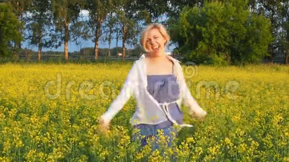一位迷人的金发女郎走过一片油菜地微笑着愉快地旋转着慢动作视频的预览图