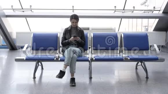机场里一位漂亮的年轻女子坐在椅子上等飞机一边用电话一边看视频的预览图