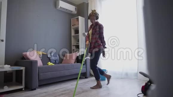 带着耳机的女人在家用拖把洗地板跳舞视频的预览图