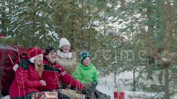 圣诞假期戴着红帽子的幸福家庭在白雪森林里休息妈妈爸爸女儿和儿子一起玩视频的预览图