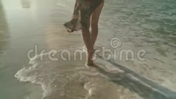 在夏天的海滩上年轻女子沿着海水和沙子散步闭上双腿旅行概念视频的预览图