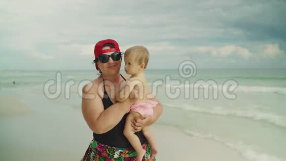 快乐的祖母在海滩上抱着她的小孙子背景是大海视频的预览图