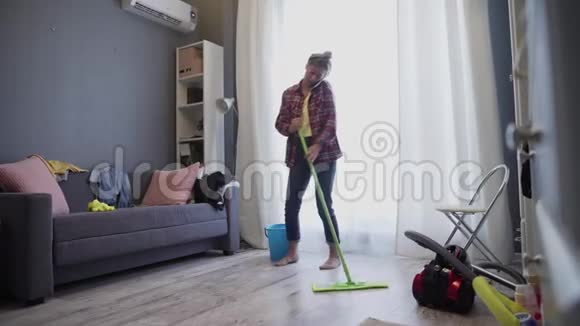 一个女人正在用拖把洗地板和打电话视频的预览图