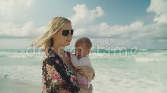 年轻的母亲抱着她的女婴沿着海滩散步天空和海洋的背景巴拿马城市海滩视频的预览图