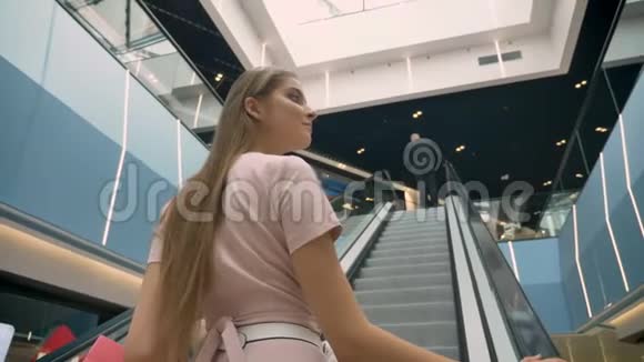 年轻漂亮的女孩站在商场的自动扶梯上拿着包购物理念时尚理念视频的预览图