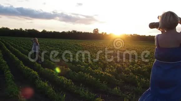 摄影师一个女人在日落时在田野里拍摄一个十几岁的女孩视频的预览图