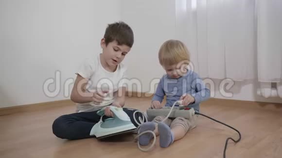 好奇的孩子们玩危险的东西弟弟们坐在地板上研究电熨斗和插座视频的预览图