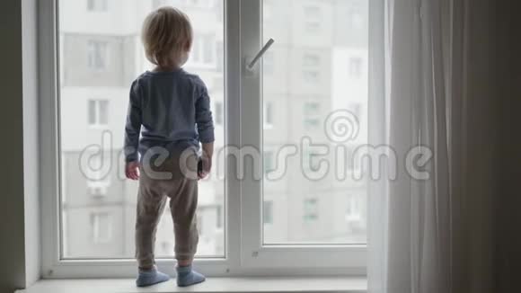 孩子在家的危险处境小男孩站在窗台上手里拿着玩具车望着窗外视频的预览图
