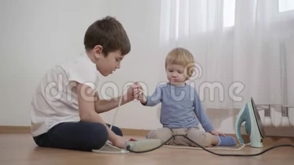 孩子有危险男孩教小哥哥打开和关闭坐在地板上的电插座上的熨斗视频的预览图