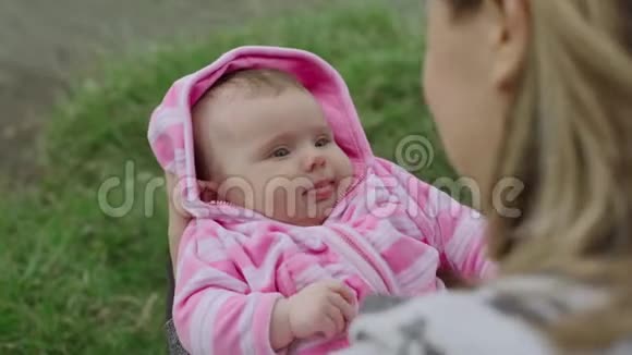 妈妈手上的小女婴在绿色的夏季公园绿色的背景下放松视频的预览图