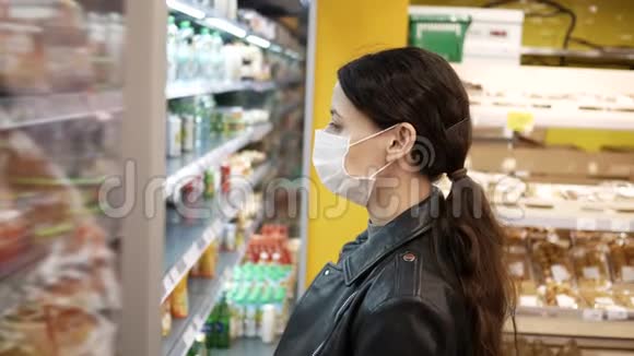 超市里戴着医用口罩的漂亮黑发年轻女子大流行选择产品视频的预览图