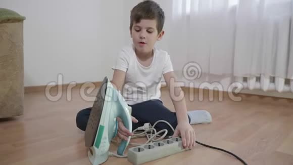孩子在客厅里冒着意外的危险小男孩在地板上玩熨斗和电动延长线视频的预览图