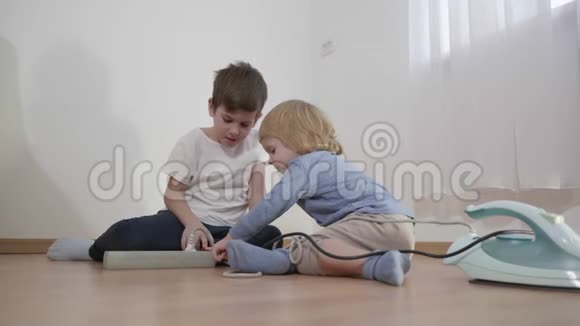 孩子们玩危险的延长线小男孩连接电线插头从铁到插座在房间的地板上视频的预览图
