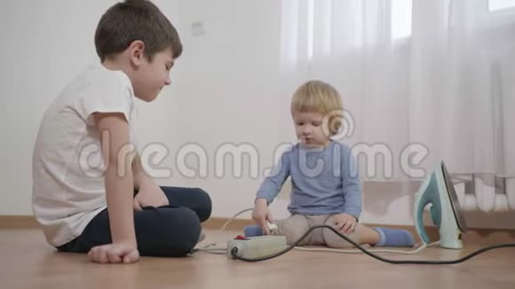危险的游戏好奇的小男孩们把电插头从铁插头插进多个插座坐在室内地板上视频的预览图