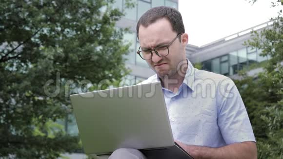 喜剧情感年轻的商人怀着厌恶的情绪在公园里拿着笔记本电脑视频的预览图