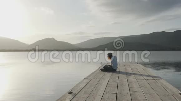 网络自由职业选择概念一位年轻女性在日落时分坐在湖边的码头上的笔记本电脑上工作视频的预览图