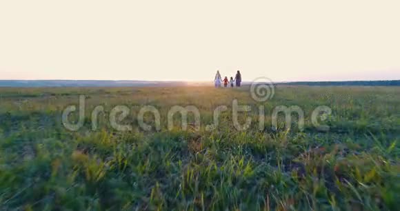 夕阳西下两个带着女儿的母亲手牵着手在田野里散步空中观景视频的预览图
