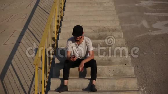 年轻人对新消息很满意坐在城市的楼梯上用智能手机聊天视频的预览图