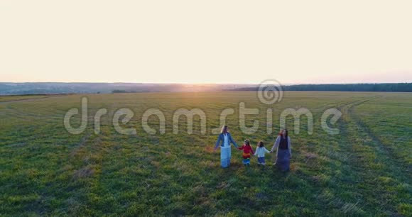 夕阳西下两个带着女儿的母亲手牵着手在田野里散步空中观景视频的预览图