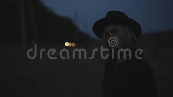 晚上街上年轻金发女孩的深色肖像戴着黑色帽子和外套视频的预览图