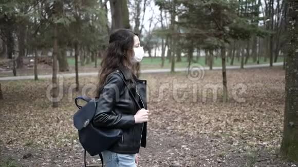 美丽的年轻女子戴着防护面具在城市公园散步流行冠状病毒视频的预览图