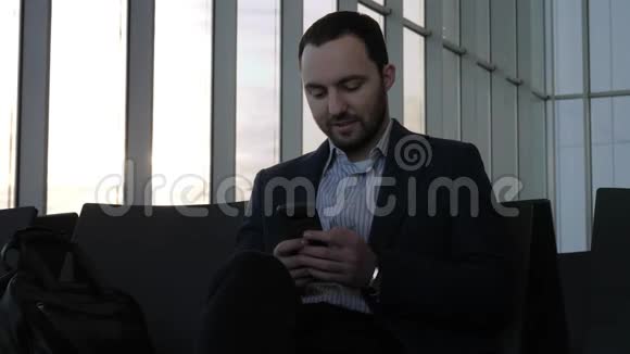 商务人员坐在机场大厅时通过手机发信息视频的预览图