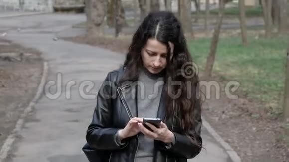 在城市公园里年轻女子用手机看新闻视频的预览图