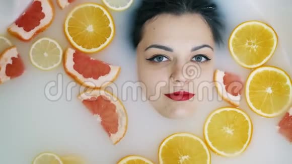 在充满水果的奶浴中美丽的女人脸的特写肖像视频的预览图